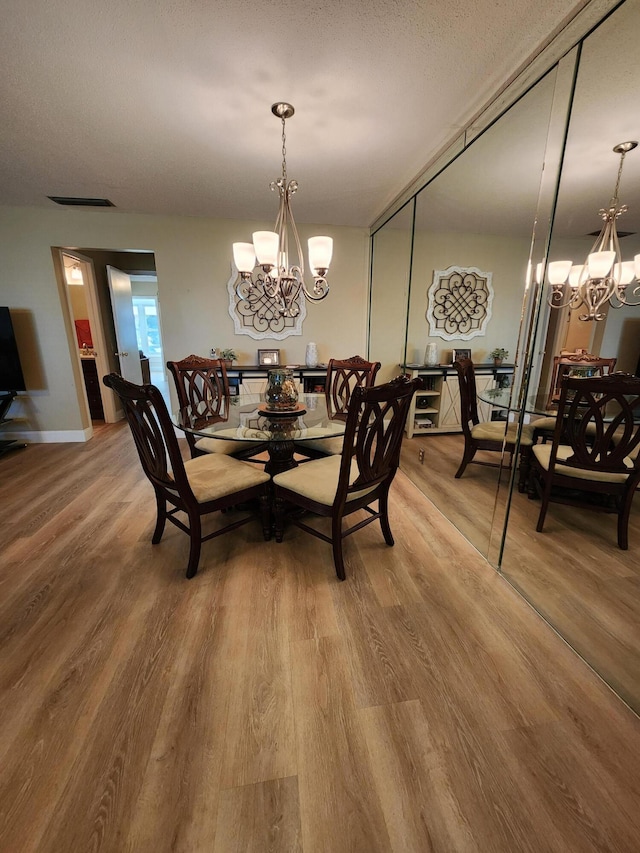 dining space featuring wood-type flooring, a textured ceiling, and a notable chandelier