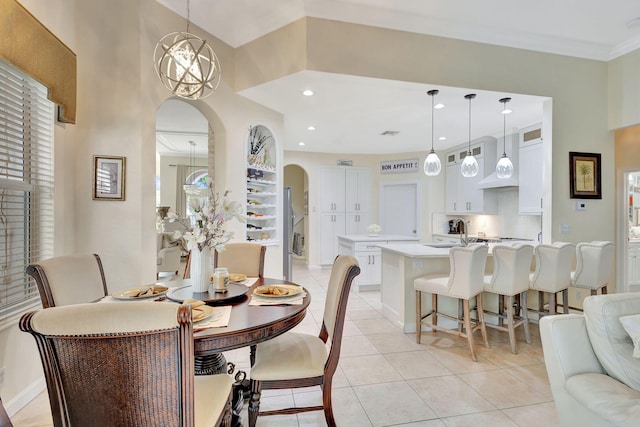 dining space with a towering ceiling, ornamental molding, sink, light tile patterned floors, and a notable chandelier