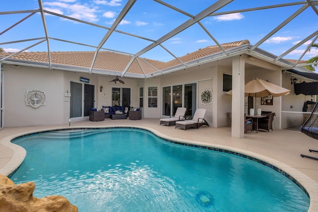 view of pool featuring outdoor lounge area, a patio, glass enclosure, and ceiling fan