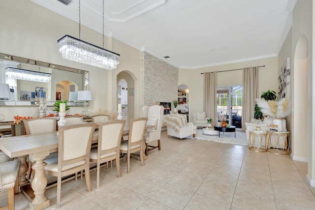 tiled dining space with a notable chandelier, a stone fireplace, and ornamental molding