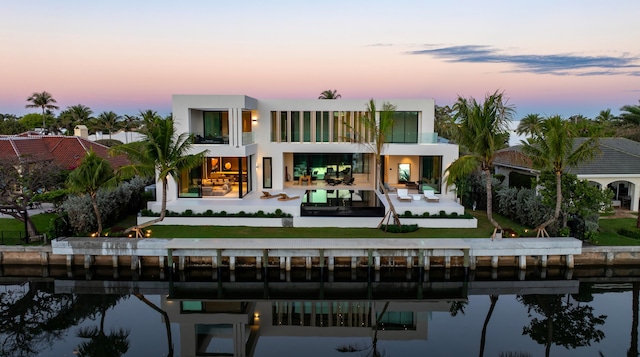 back of house at dusk with a yard, stucco siding, a water view, a patio area, and a balcony