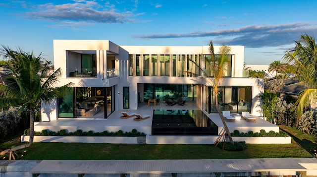 back of property at dusk featuring a yard, a patio, a balcony, and stucco siding