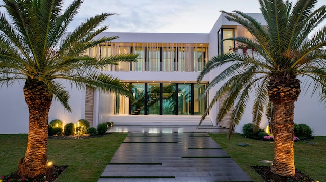 rear view of property featuring a lawn, a balcony, and stucco siding