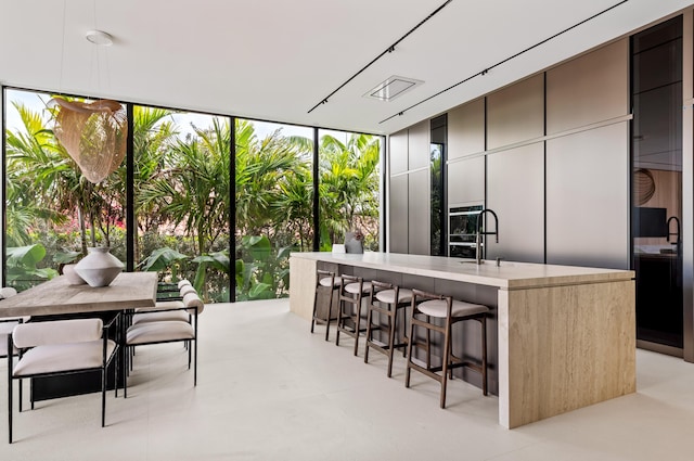 kitchen featuring a breakfast bar area, a kitchen island with sink, a sink, a wall of windows, and modern cabinets