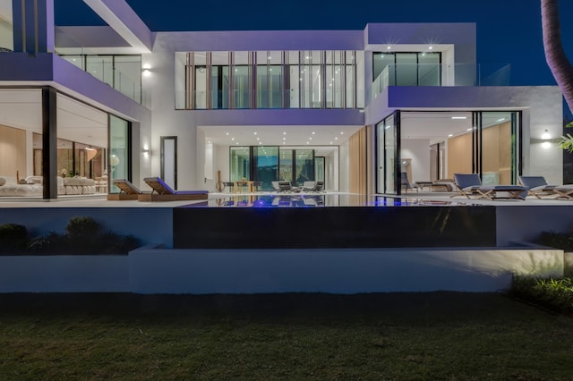 35 Spoonbill Rd, Manalapan, FL 33462 - back of house at night featuring a balcony, stucco siding, and a patio area