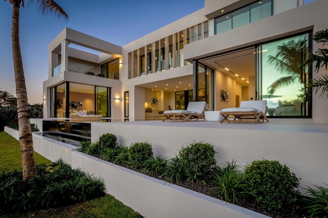 back of property at dusk featuring a balcony and stucco siding