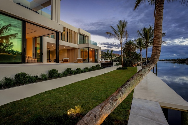 yard at dusk with a water view, a balcony, and a dock