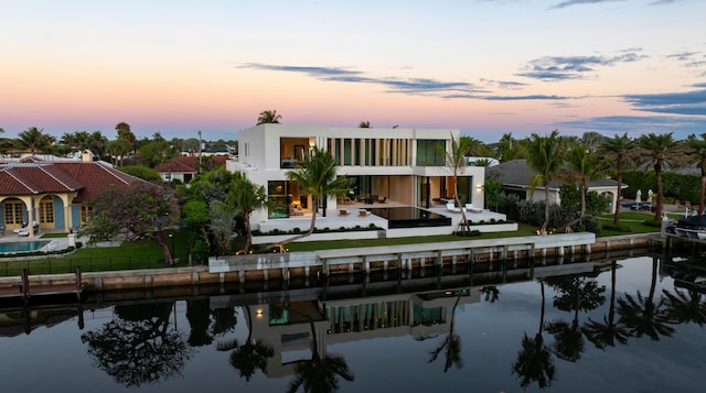 back of house at dusk featuring a yard, a water view, and a balcony