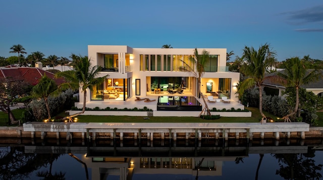 rear view of property with a patio, a balcony, a water view, a yard, and stucco siding