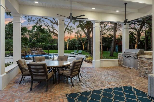 patio terrace at dusk featuring grilling area, ceiling fan, and exterior kitchen