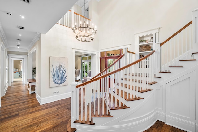 stairway with an inviting chandelier, hardwood / wood-style floors, a towering ceiling, and ornamental molding