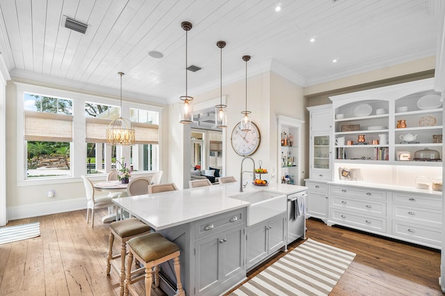 kitchen with a kitchen bar, sink, crown molding, hanging light fixtures, and a center island with sink