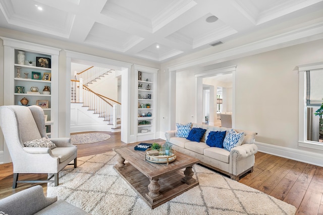 living room with built in shelves, coffered ceiling, hardwood / wood-style flooring, ornamental molding, and beamed ceiling