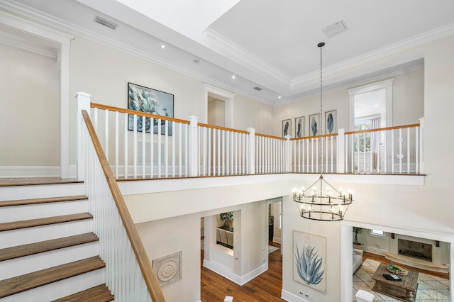 staircase featuring crown molding, wood-type flooring, a chandelier, and a towering ceiling