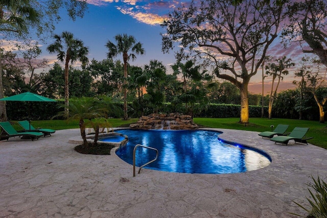 pool at dusk featuring a patio, pool water feature, a yard, and an in ground hot tub