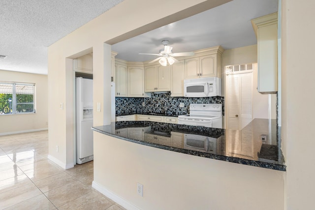 kitchen with kitchen peninsula, cream cabinets, white appliances, and dark stone counters