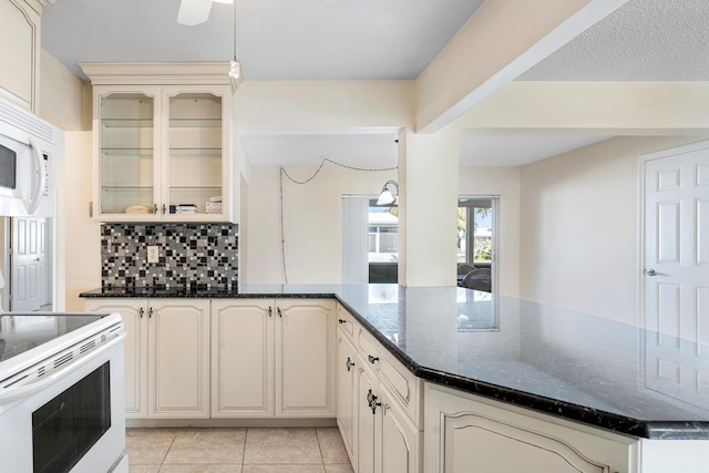 kitchen featuring tasteful backsplash, dark stone counters, white appliances, cream cabinetry, and light tile patterned flooring