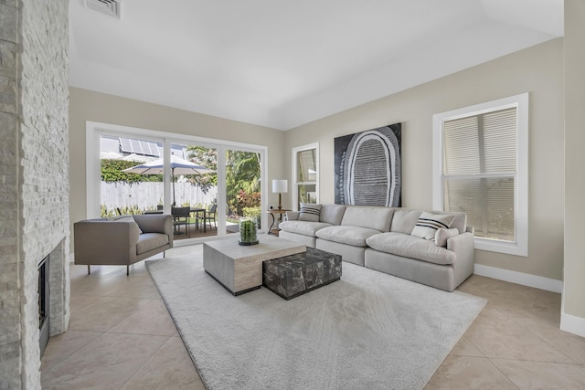 living area featuring a stone fireplace, light tile patterned flooring, visible vents, and baseboards