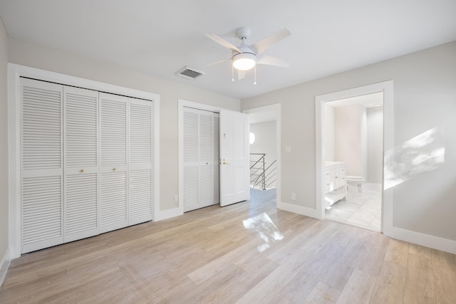 unfurnished bedroom with ceiling fan, ensuite bathroom, two closets, and light wood-type flooring