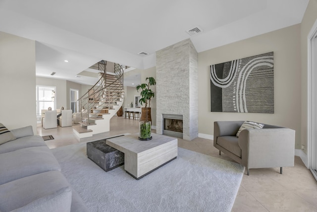 living room featuring light tile patterned floors, a stone fireplace, visible vents, baseboards, and stairway