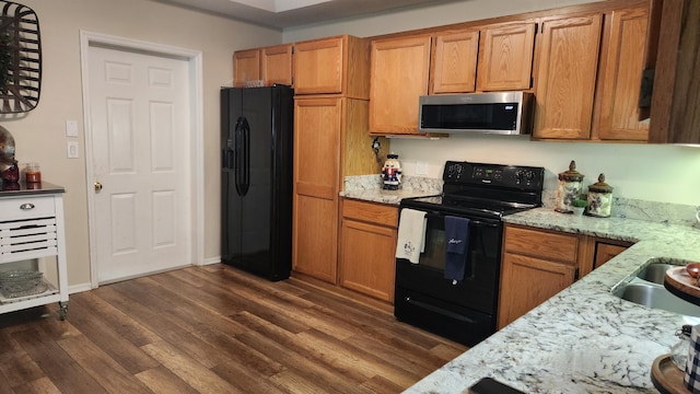 kitchen with light stone countertops, dark hardwood / wood-style floors, sink, and black appliances