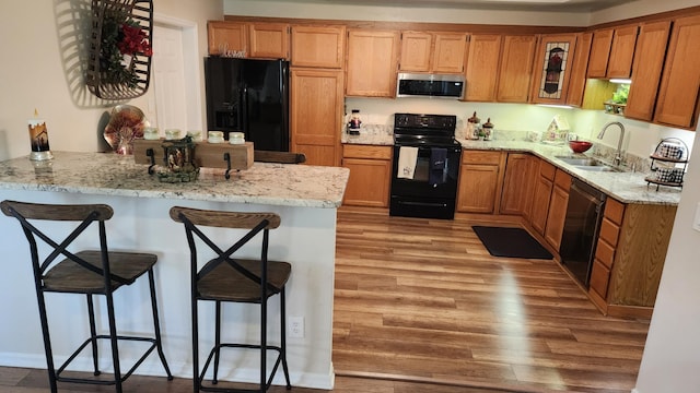 kitchen featuring kitchen peninsula, light wood-type flooring, a breakfast bar, sink, and black appliances