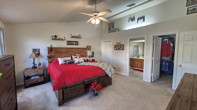 bedroom with ensuite bathroom, a walk in closet, light carpet, a textured ceiling, and a closet