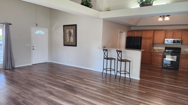 kitchen featuring a breakfast bar area, light stone counters, high vaulted ceiling, dark hardwood / wood-style flooring, and black appliances