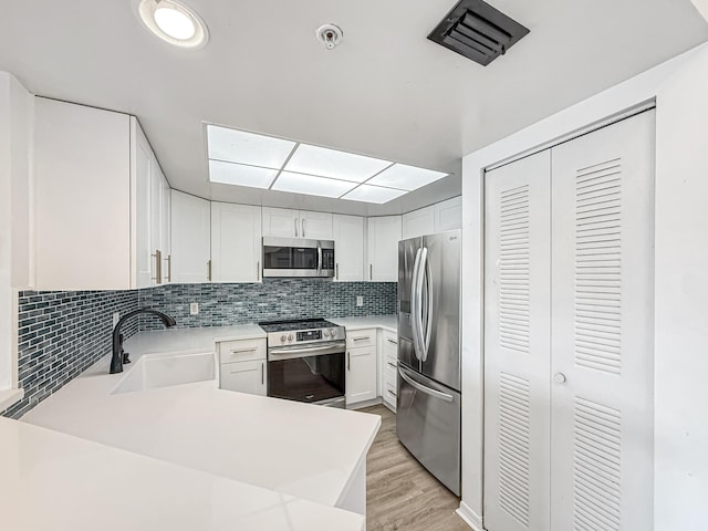 kitchen with white cabinets, decorative backsplash, appliances with stainless steel finishes, light countertops, and a sink