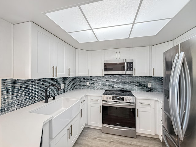 kitchen with light wood finished floors, light countertops, appliances with stainless steel finishes, white cabinetry, and a sink