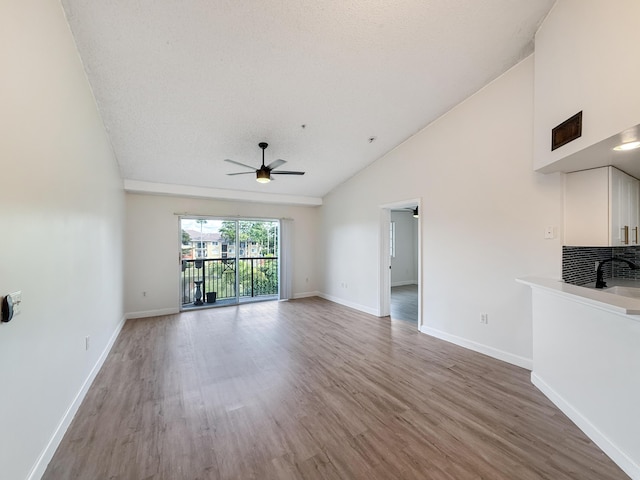 unfurnished living room featuring ceiling fan, high vaulted ceiling, a textured ceiling, wood finished floors, and baseboards