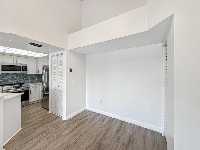 kitchen featuring tasteful backsplash, light countertops, appliances with stainless steel finishes, light wood-style floors, and white cabinetry