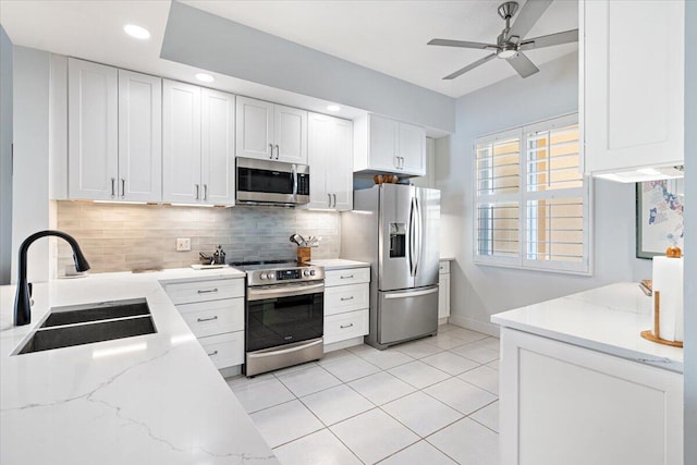 kitchen with white cabinets, appliances with stainless steel finishes, light stone countertops, and sink