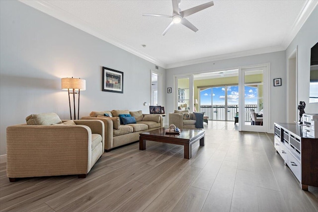 living room featuring ceiling fan, ornamental molding, a textured ceiling, and light wood-type flooring