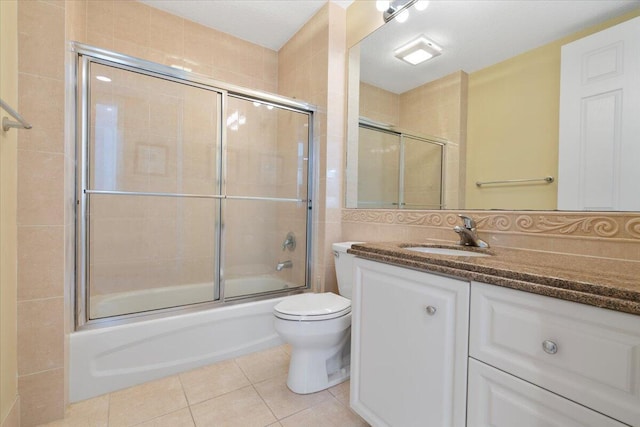 full bathroom featuring vanity, tile patterned floors, bath / shower combo with glass door, toilet, and a textured ceiling