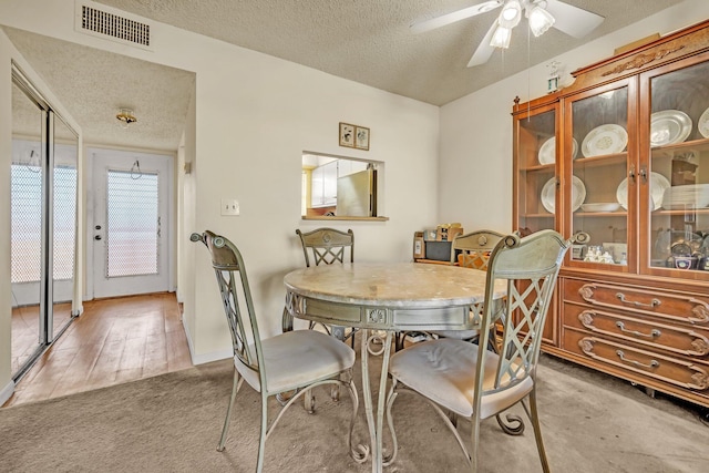 dining area with ceiling fan, light wood-type flooring, and a textured ceiling