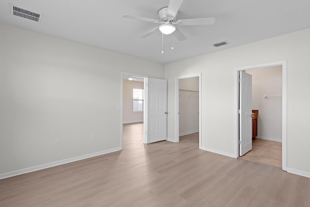 unfurnished bedroom featuring a walk in closet, ceiling fan, ensuite bath, and light hardwood / wood-style floors