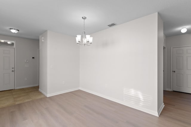 unfurnished room with light wood-type flooring and an inviting chandelier