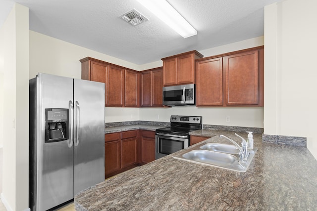 kitchen with kitchen peninsula, sink, stainless steel appliances, and a textured ceiling