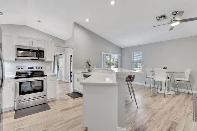 kitchen featuring white cabinets, a kitchen breakfast bar, appliances with stainless steel finishes, and vaulted ceiling