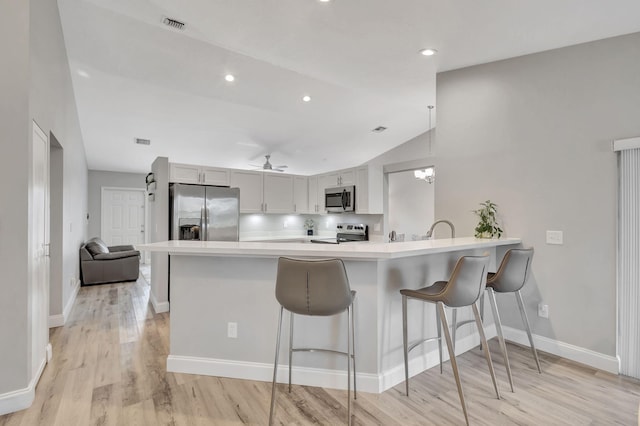 kitchen featuring lofted ceiling, light wood-type flooring, appliances with stainless steel finishes, kitchen peninsula, and a breakfast bar area