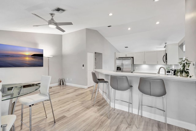 kitchen with kitchen peninsula, light wood-type flooring, stainless steel appliances, sink, and white cabinetry