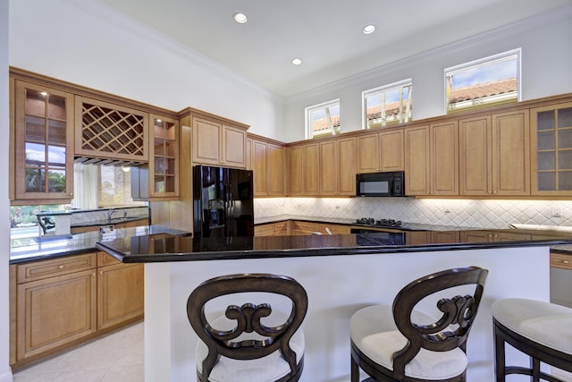 kitchen with dark stone countertops, a kitchen bar, ornamental molding, light tile patterned floors, and black appliances