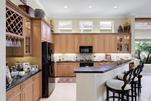 kitchen with light tile patterned floors, crown molding, black appliances, and a kitchen breakfast bar