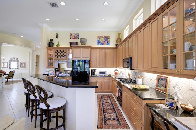 kitchen featuring light tile patterned floors, a breakfast bar area, backsplash, ornamental molding, and black appliances