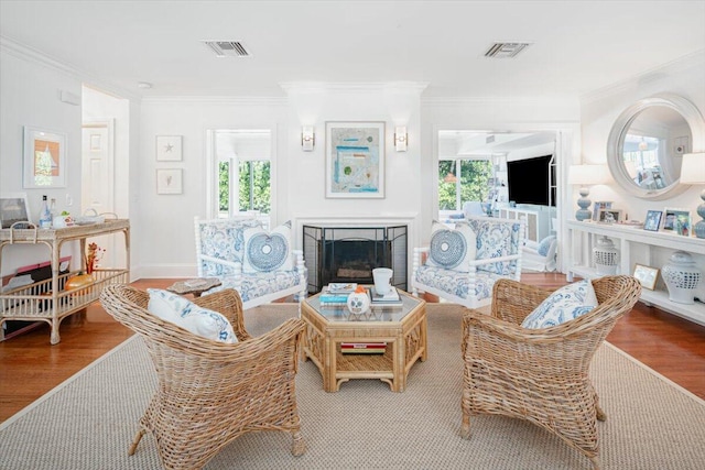 living room with crown molding, plenty of natural light, wood-type flooring, and a brick fireplace