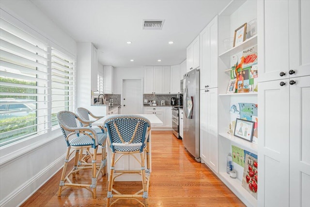 kitchen with sink, tasteful backsplash, light hardwood / wood-style floors, white cabinets, and appliances with stainless steel finishes