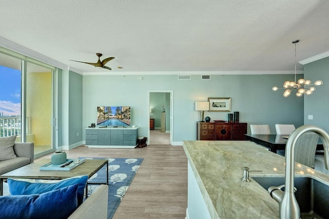 interior space featuring ceiling fan with notable chandelier, light wood-type flooring, ornamental molding, and sink