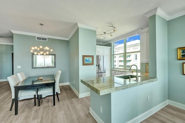 kitchen with kitchen peninsula, sink, decorative light fixtures, white cabinets, and stainless steel fridge with ice dispenser