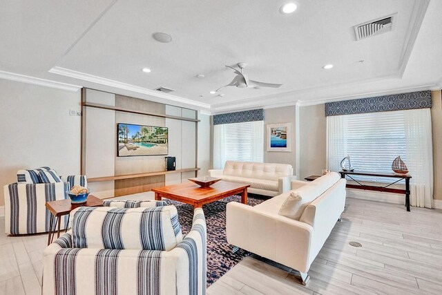 living room with ceiling fan, light hardwood / wood-style floors, ornamental molding, and a tray ceiling